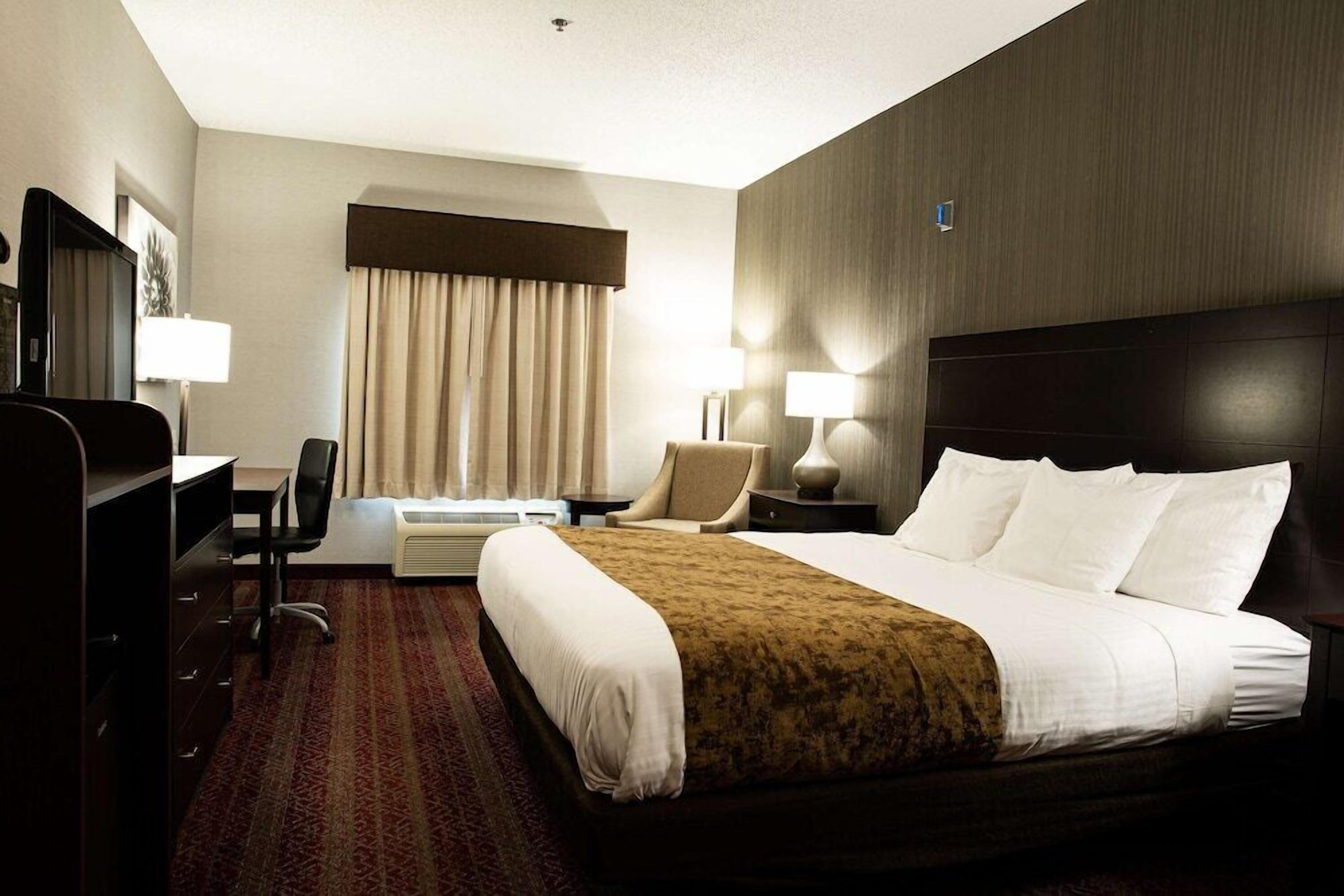 A hotel room with a bed, desk, chair, and a large window with curtains.