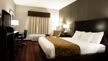 A hotel room with a large bed, a desk, a chair, two bedside tables with lamps, a TV, and a window with curtains.