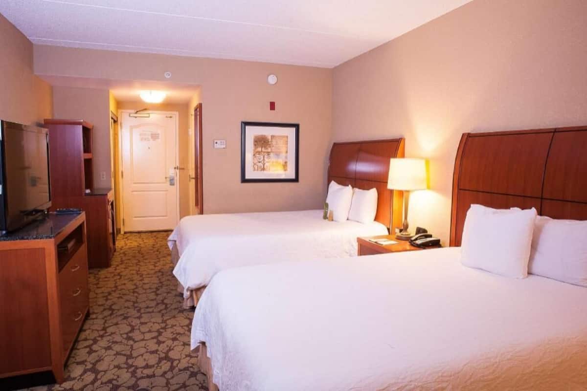 A hotel room with two beds, a desk, a television, and a framed picture on the wall.