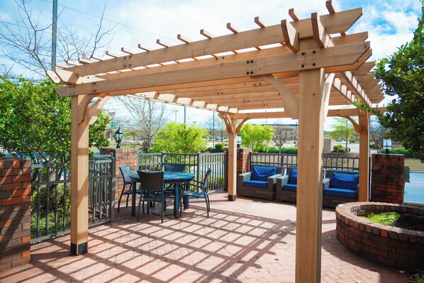 Un patio exterior con una pérgola de madera, zona de estar y suelo de ladrillo.