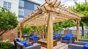 An outdoor patio area with wicker furniture and a wooden pergola. - Hilton Garden Inn Hattiesburg (Hattiesburg)