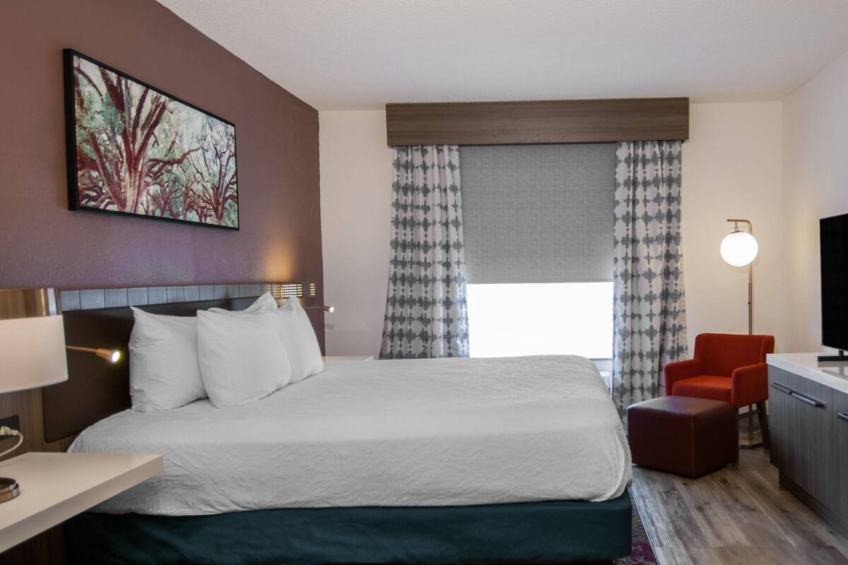 A hotel room with a large bed, a desk with a chair, a TV, and a painting on the wall.