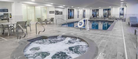 Zona de piscina interior de hotel con jacuzzi, asientos y señales de seguridad.