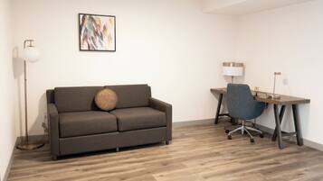 A modern room with a grey sofa, a desk with a chair, and a floor lamp.