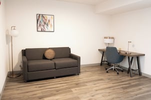 Una habitación moderna con un sofá gris, un escritorio con una silla y una lámpara de pie.