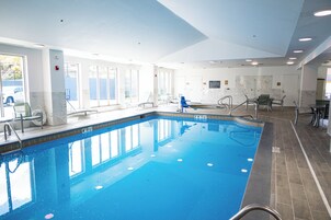 Una amplia piscina interior con agua cristalina, rodeada de suelo y paredes con azulejos, y equipada con múltiples puntos de acceso y salida.