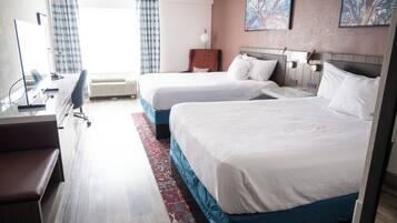 A hotel room with two beds, a desk with a chair, a large window with curtains, and artwork on the wall.