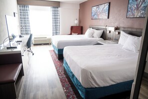 Habitación de hotel con dos camas, un escritorio con silla, un ventanal con cortinas y una obra de arte en la pared.