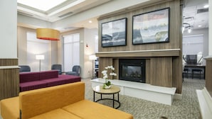 A modern hotel lobby with a fireplace, seating area, and artwork on the wall. - Hilton Garden Inn Hattiesburg (Hattiesburg)