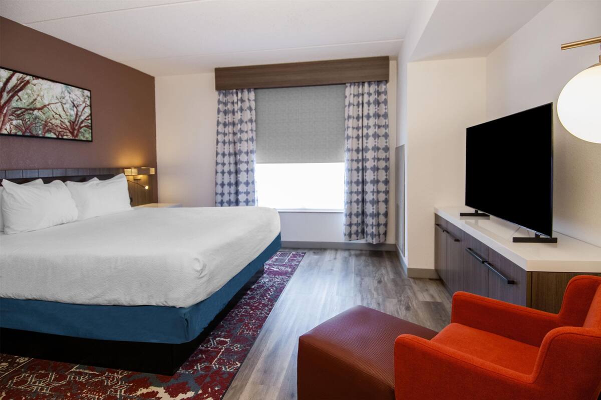 A hotel room with a large bed, a television, a desk, and a window with curtains.
