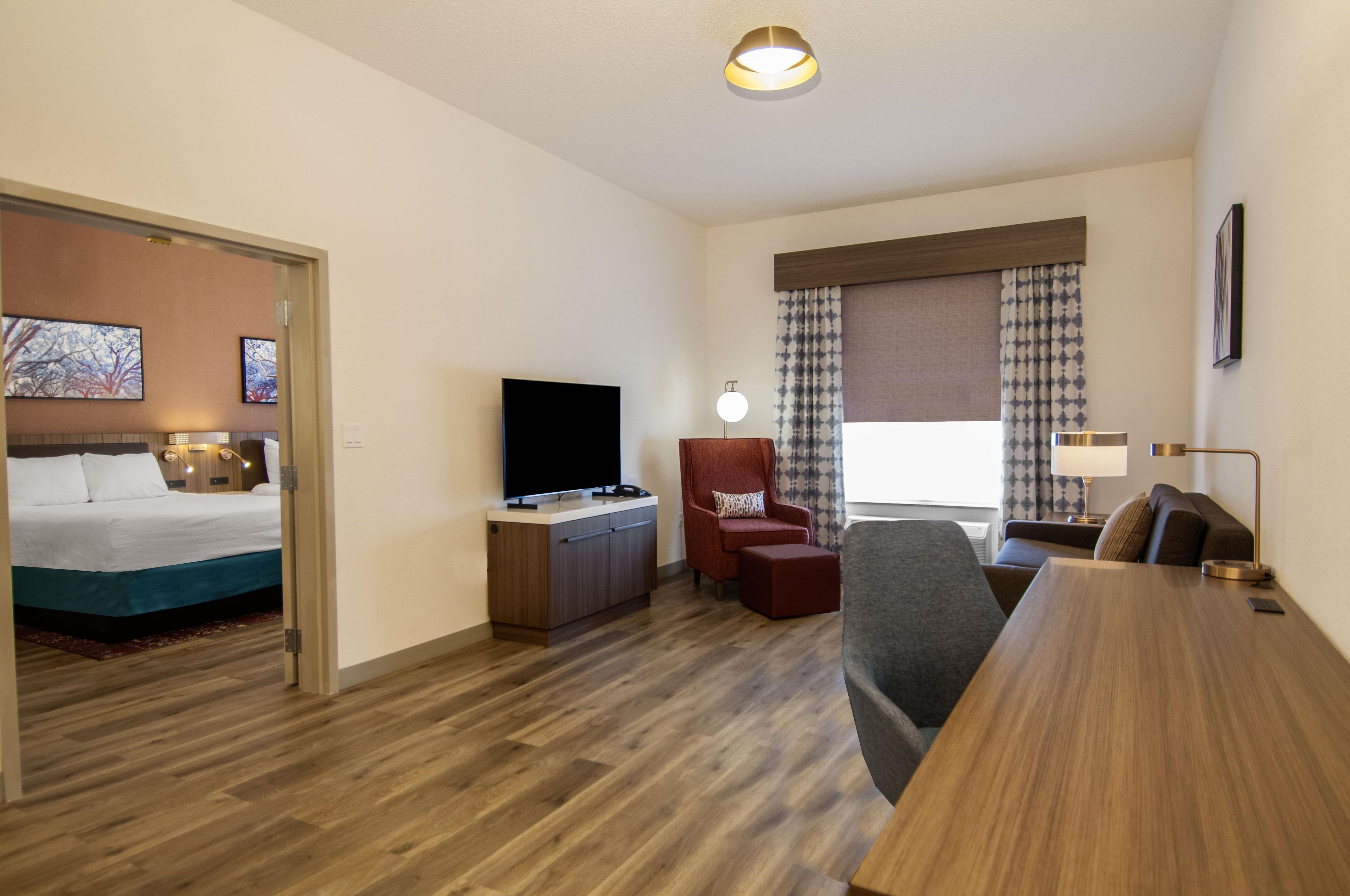 Ein Hotelzimmer mit Bett, Fernseher, Schreibtisch, Stuhl und einem fenster mit Vorhängen.