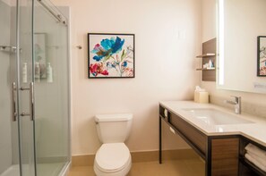 Un baño con cabina de ducha de vidrio, inodoro, lavamanos y espejo.