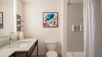 Casa de banho com sanita, lavatório e chuveiro. Há uma moldura com uma ilustração floral na parede.