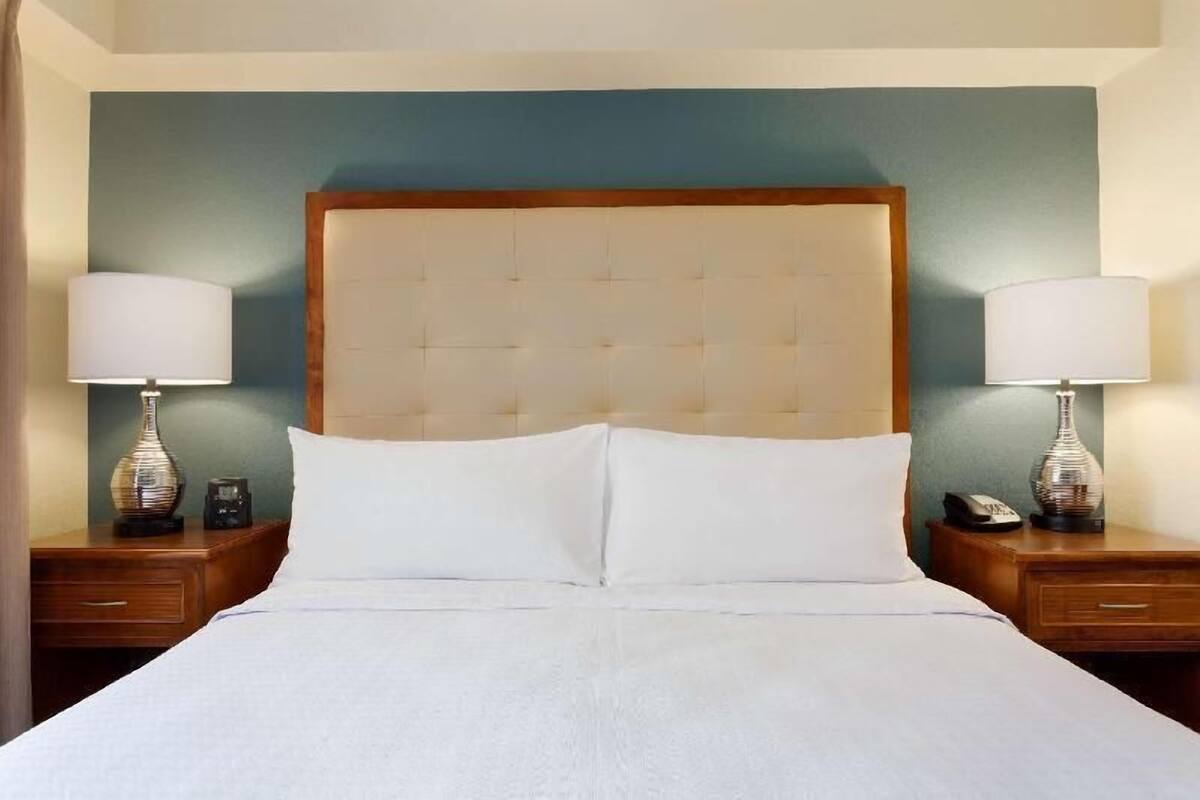 Une chambre d’hôtel avec un grand lit, deux tables de chevet avec des lampes, une tête de lit en bois et un mur d’accent bleu.