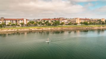 Un plan d’eau sur lequel une personne pratique le paddle, entouré d’un ensemble d’immeubles à plusieurs étages, surmontés d’un toit recouvert de tuiles rouges.