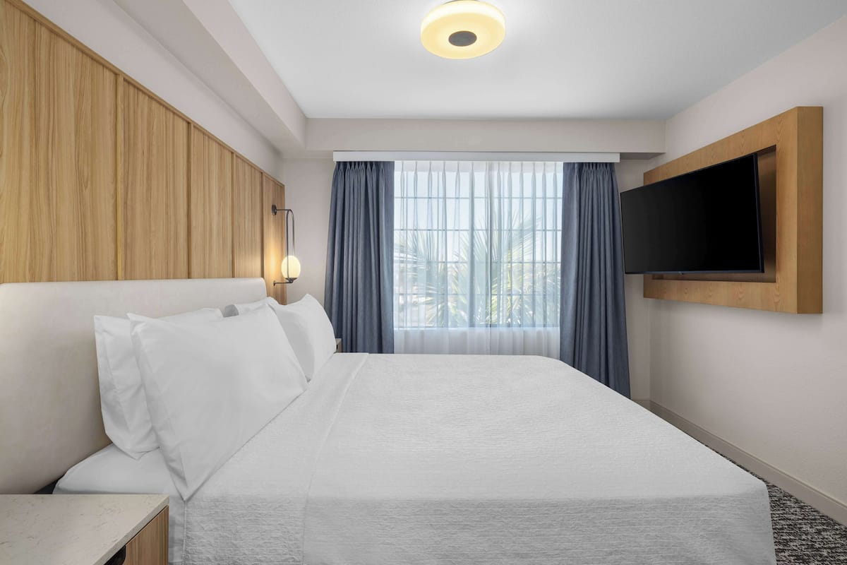 Une chambre d’hôtel avec un grand lit, un téléviseur à écran plat fixé au mur, une fenêtre avec des rideaux et un luminaire au plafond.