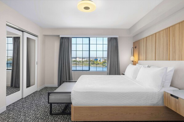 Habitación de hotel con una cama grande, un escritorio, una silla y vistas a un lago, además de una puerta corredera.