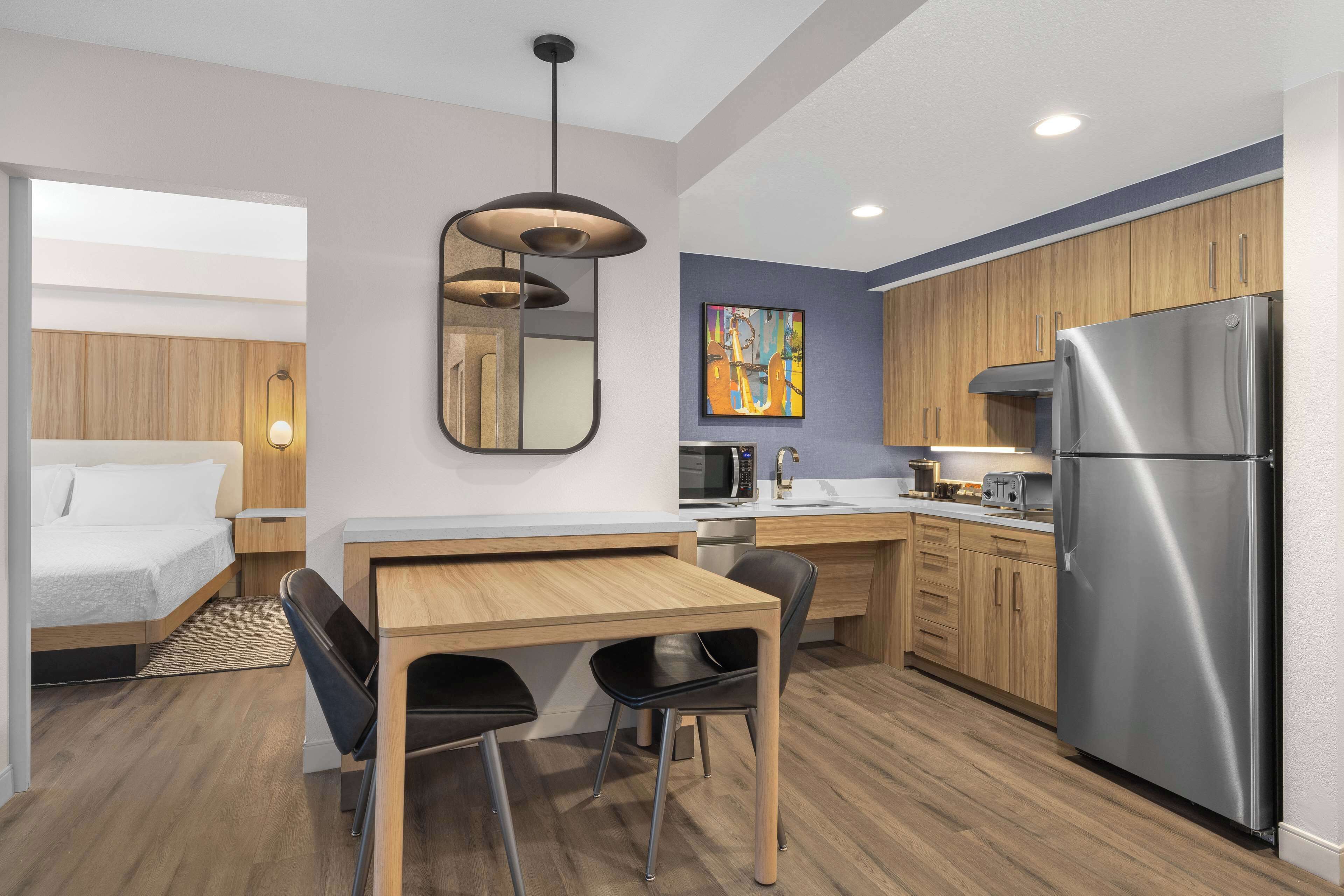 Una cocina compacta con armarios de madera, un refrigerador de acero inoxidable, un microondas y una zona de comedor con mesa y sillas.
