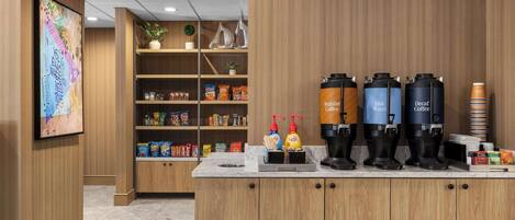 A coffee station with dispensers labeled 'Regular Coffee,' 'Hot Water,' and 'Decaf Coffee,' along with a variety of snacks and condiments.