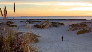 Uma praia com dunas de areia e uma pessoa caminhando.