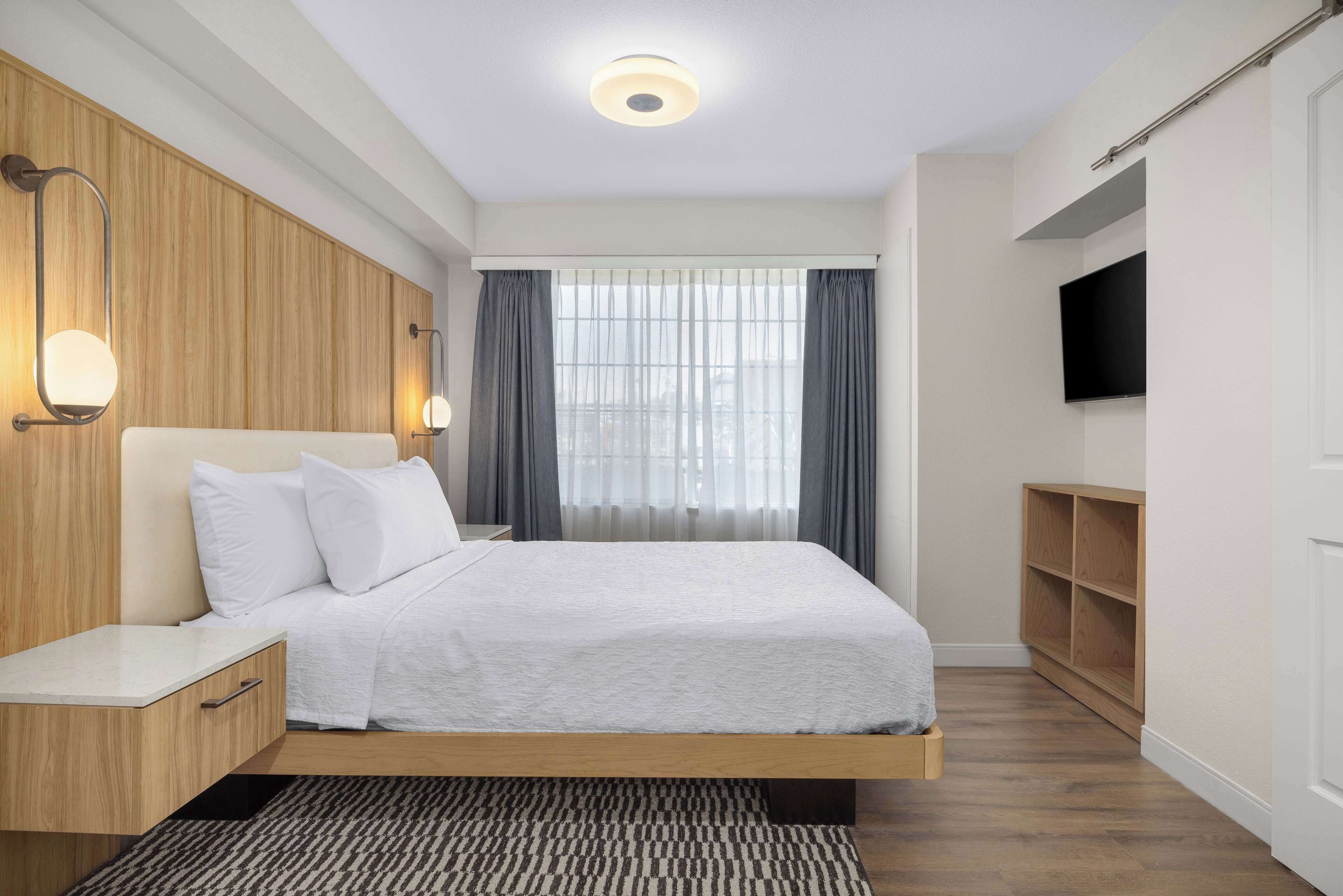A modern bedroom with a bed, bedside tables, a TV, and a wooden wardrobe.