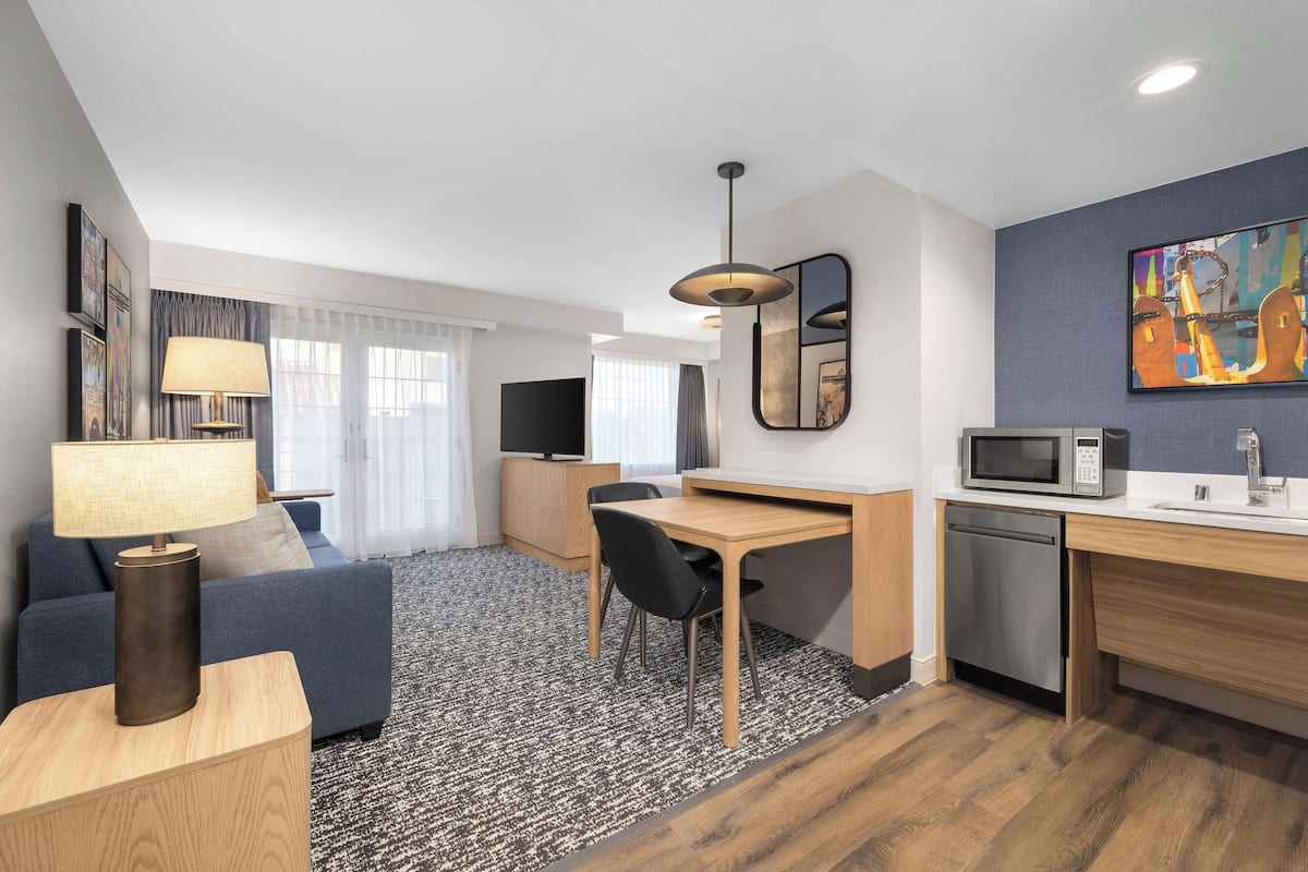 Une chambre d’hôtel moderne équipée d’un canapé, d’un bureau, d’une table à manger, d’une lampe, d’une télévision, d’un four à micro-ondes et d’un lave-vaisselle.