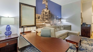 A hotel room with a large desk, a sofa, a small table, and a decorative mirror. - Clarion Pointe Sulphur Springs (Sulphur Springs)