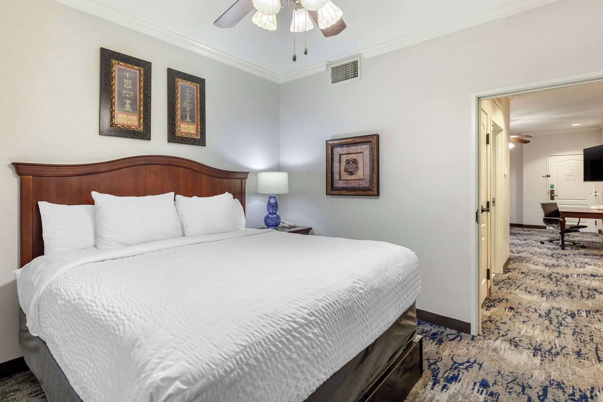 A hotel room with a large bed, a nightstand with a lamp, and framed pictures on the wall.