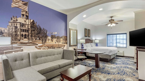 A hotel room with a large bed, a sofa, a desk, and a television. - Clarion Pointe Sulphur Springs (Sulphur Springs)