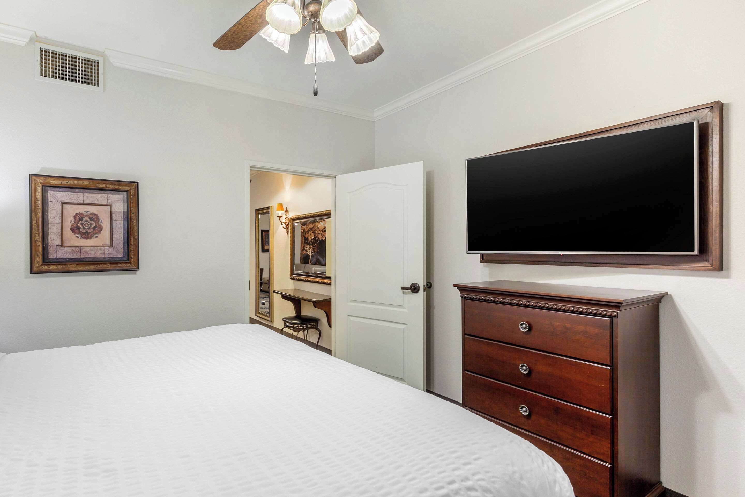 A bedroom with a bed, a dresser, a television on the wall, and a door leading to another room.