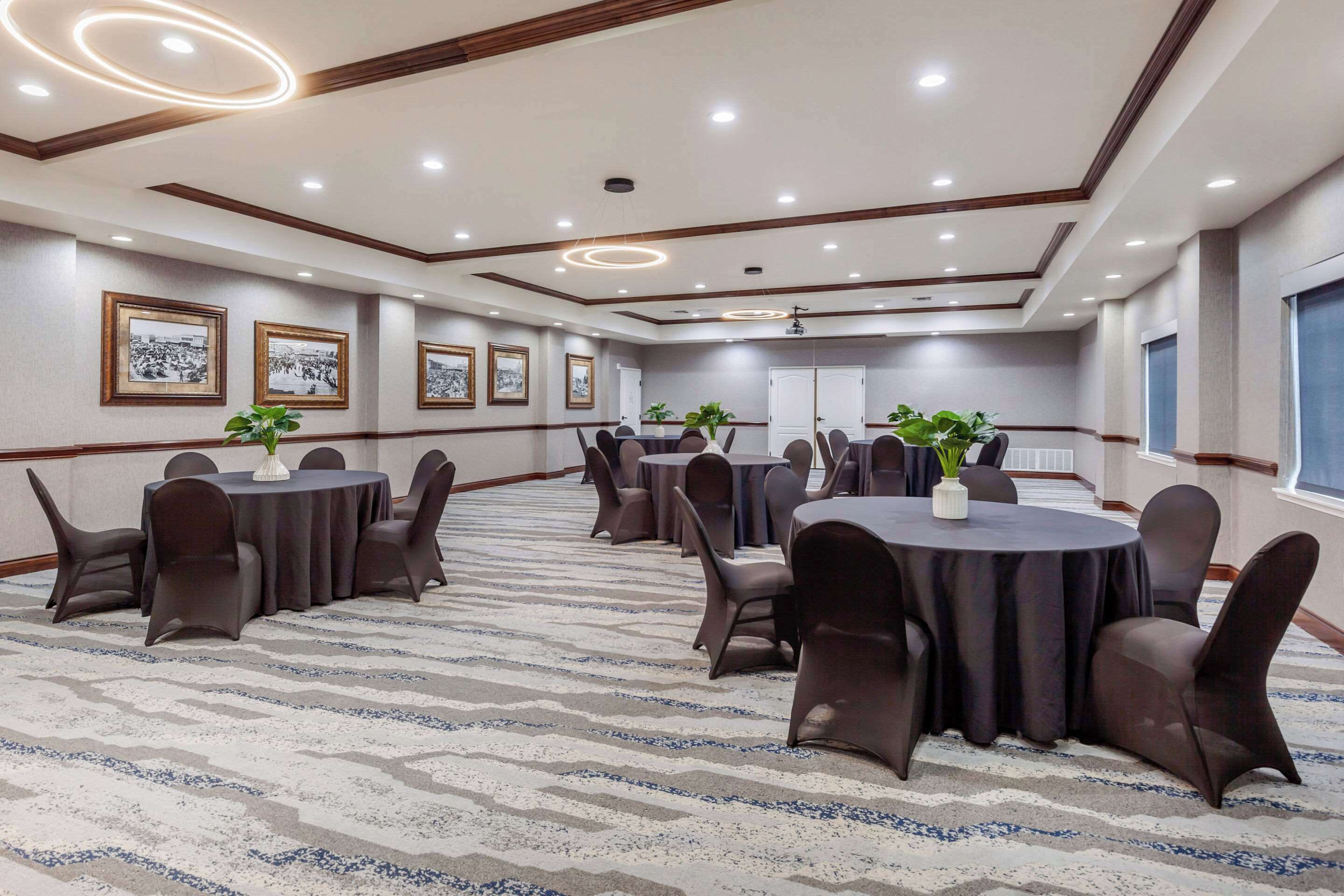 A conference room with multiple tables and chairs, framed pictures on the walls, and a carpeted floor.
