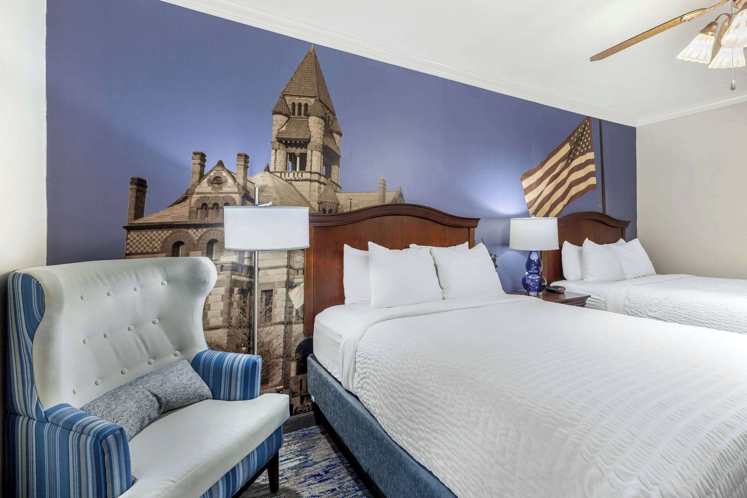 Una habitación de hotel con una cama grande, dos mesitas de noche, una silla y un mural de un edificio.