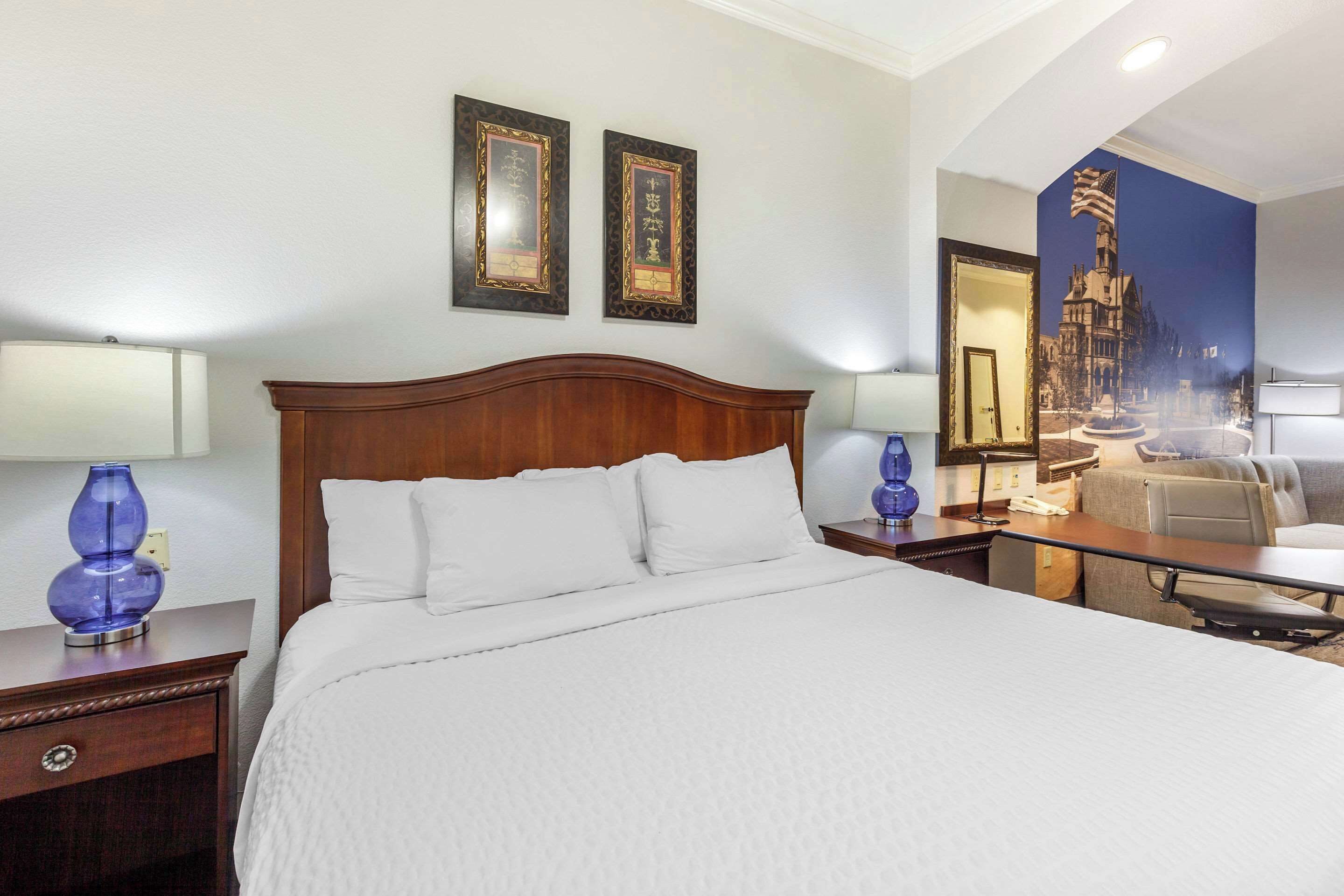 Une chambre d’hôtel avec un grand lit, deux tables de chevet avec des lampes, une commode, une chaise et un mur orné de tableaux.