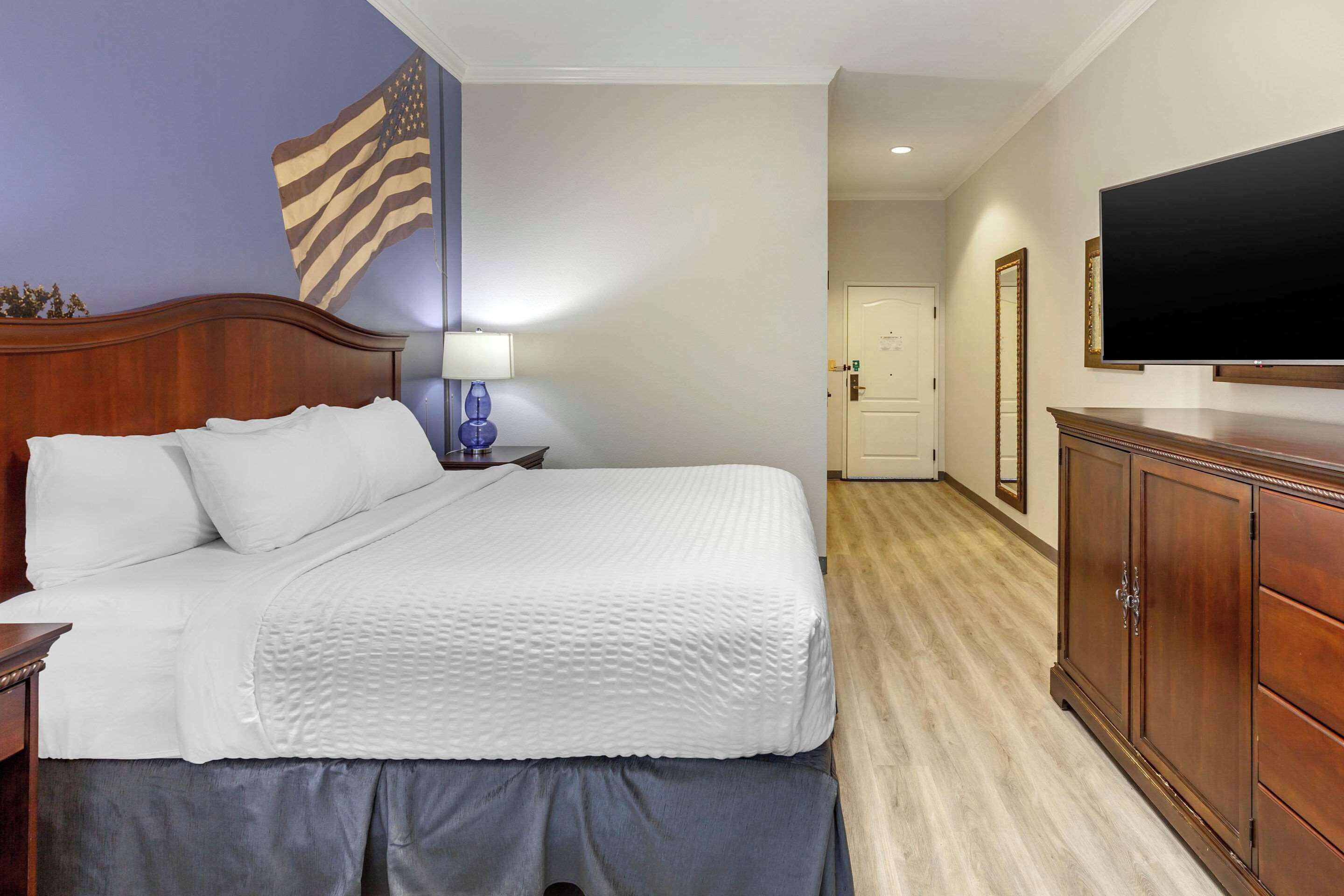 Une chambre d’hôtel avec un lit, une table de chevet, une lampe, un téléviseur, une armoire et un drapeau américain accroché au mur.