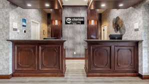 A reception area with two wooden reception desks, a patterned wall, and a sign for 'Clarion Pointe'. - Clarion Pointe Sulphur Springs (Sulphur Springs)