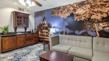 A cozy living room with a sofa, a wooden coffee table, and a kitchen area with wooden cabinets and a large window.