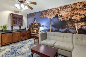 A cozy living room with a sofa, a wooden coffee table, and a kitchen area with wooden cabinets and a large window.