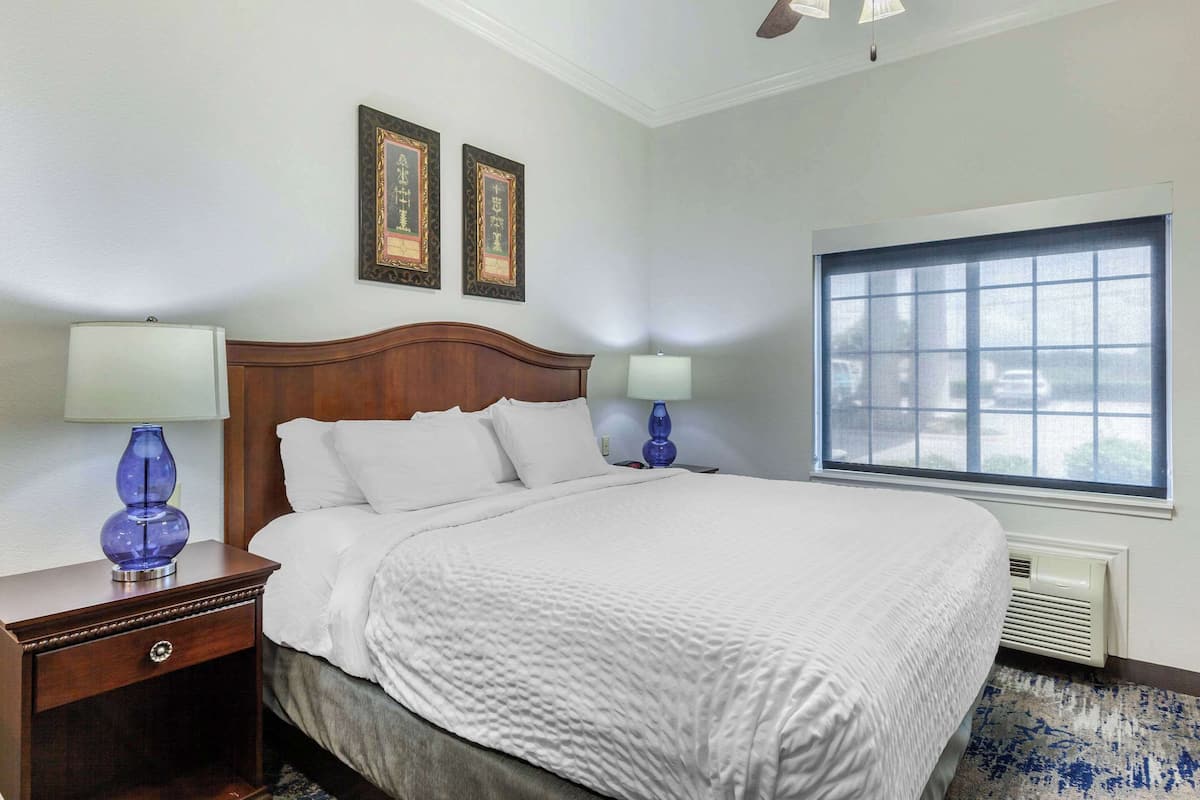 A neatly made bed with white linens, a wooden headboard, and two bedside lamps.