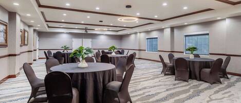 A conference room with multiple round tables, dark chairs, and potted plants.