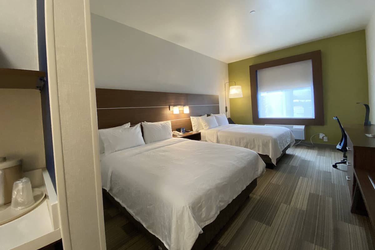 Habitación de hotel con dos camas, una mesita de noche, una lámpara y una ventana con persianas.