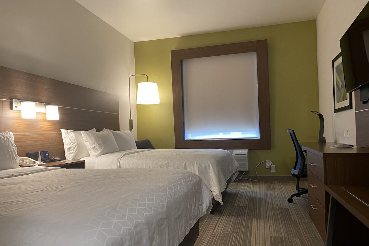 Una habitación de hotel con dos camas, un escritorio, una silla, una lámpara y un televisor.