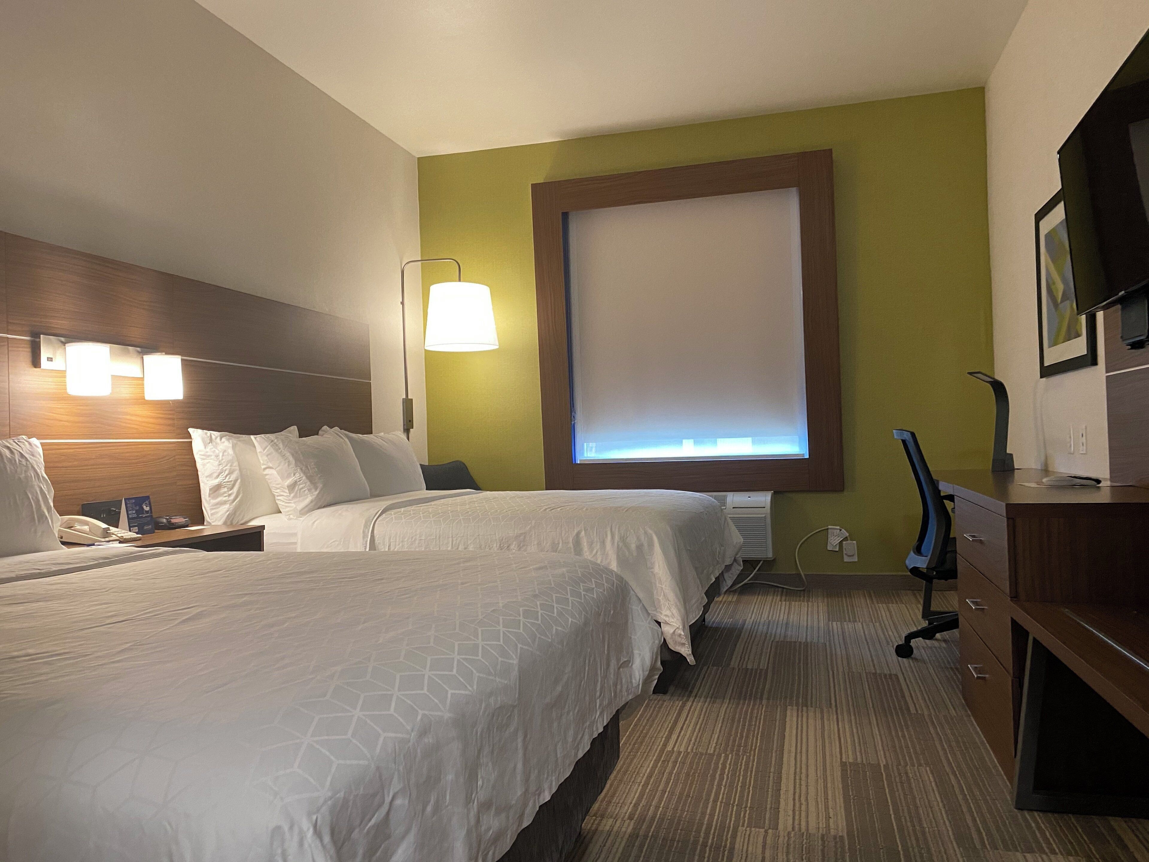 Una habitación de hotel con dos camas, un escritorio, una silla, una lámpara y un televisor.