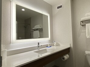A bathroom with a large mirror, a sink, a towel rack, and a shower area. - Holiday Inn Express & Suites Beaumont - Oak Valley by IHG (Beaumont)