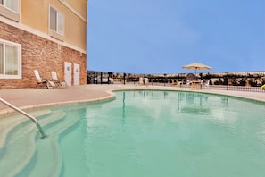 Une piscine avec des chaises longues et un espace salon abrité.