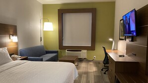 Ett hotellrum med en säng, en blå soffa, ett skrivbord med en dator, en tv och ett stort fönster.