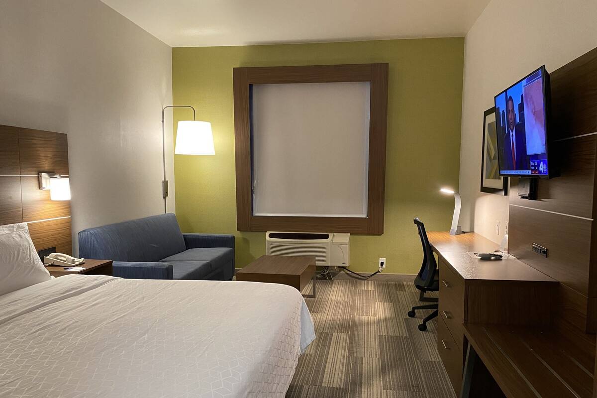 Habitación de hotel con cama, sofá azul, escritorio con computadora, televisor y ventana grande.