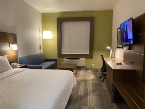 A hotel room with a bed, a blue sofa, a desk with a computer, a TV, and a large window. - Holiday Inn Express & Suites Beaumont - Oak Valley by IHG (Beaumont)