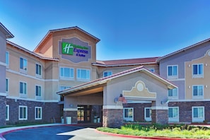 A Holiday Inn Express & Suites hotel with a central entrance, American flag, and a landscaped front yard.