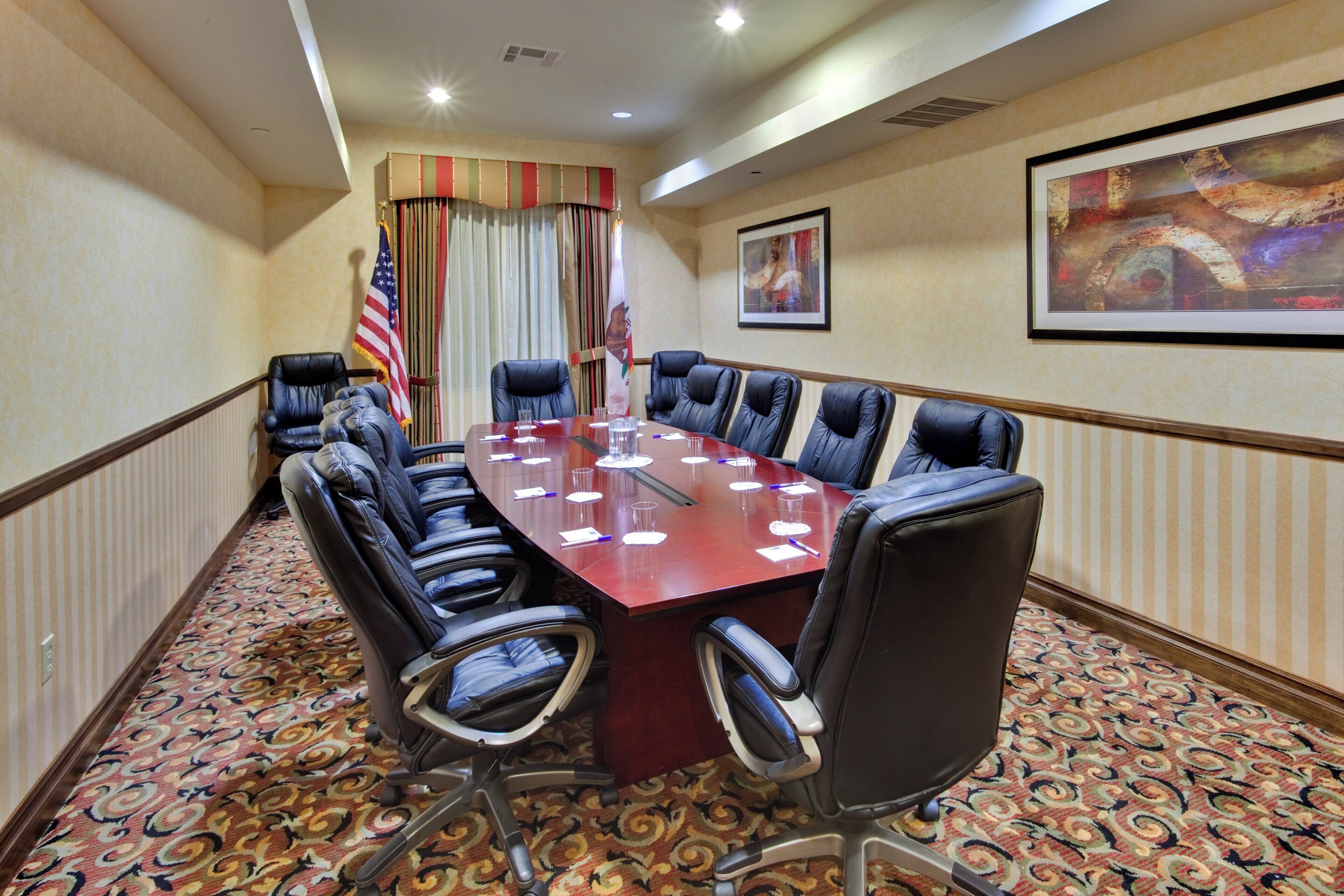 A conference room with a long table, multiple chairs, an American flag, and a painting on the wall.