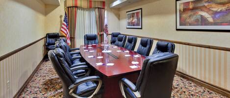 A conference room with a long table, multiple chairs, an American flag, and a painting on the wall.